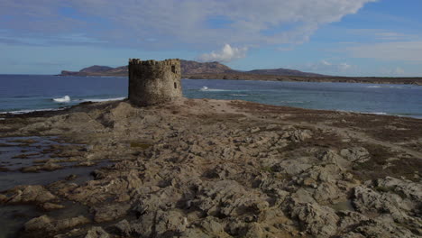 Aerial-view-in-orbit-and-at-low-altitude-over-the-tower-located-on-the-Isola-della-Pelosa,-Sardinia-on-a-sunny-day