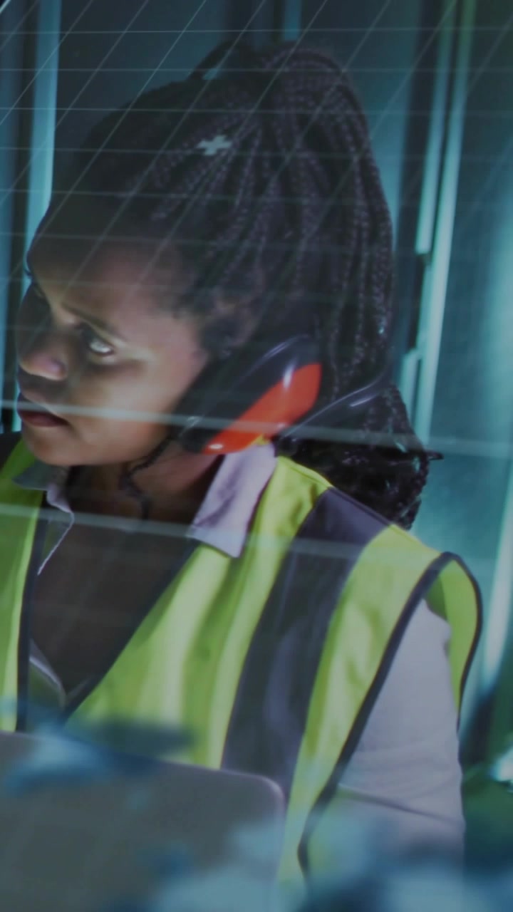 Video verticale: Un tecnico osserva un pannello, si gira e ascolta, controllando i dati dell'impianto attraverso una griglia di vetro.