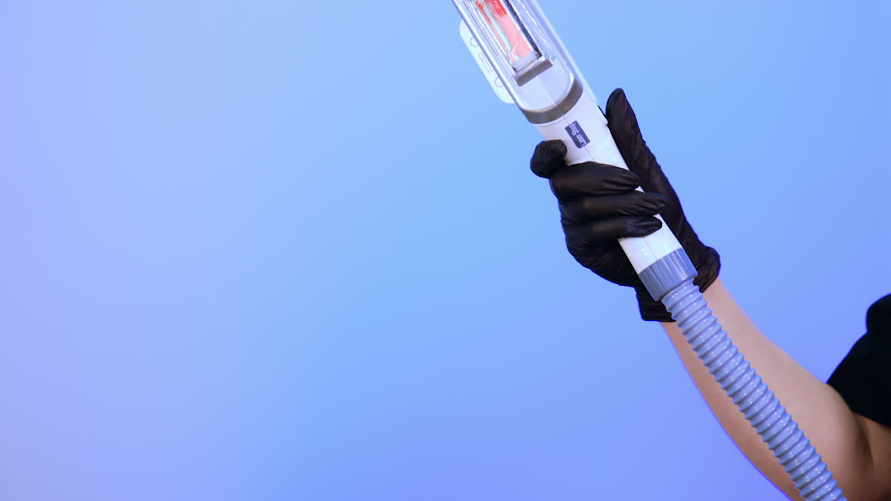 Hand in black latex gloves holds the apparatus for laser hair removal. Specialist presents the work of modern equipment. Blue backdrop.
