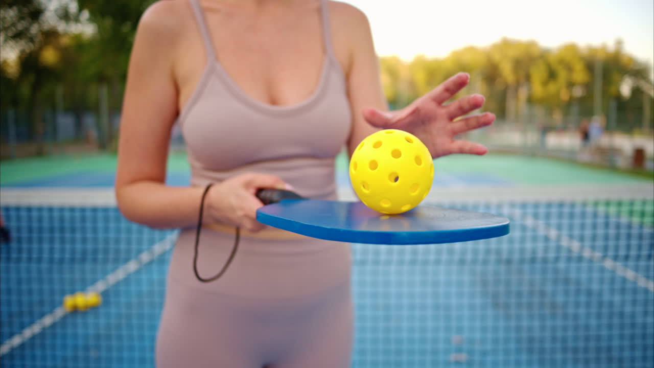 Woman playing pickleball with yellow ball and blue paddle at a court