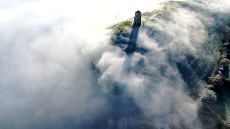 beautiful shot of glastonbury tor, shadows cast across passing mists