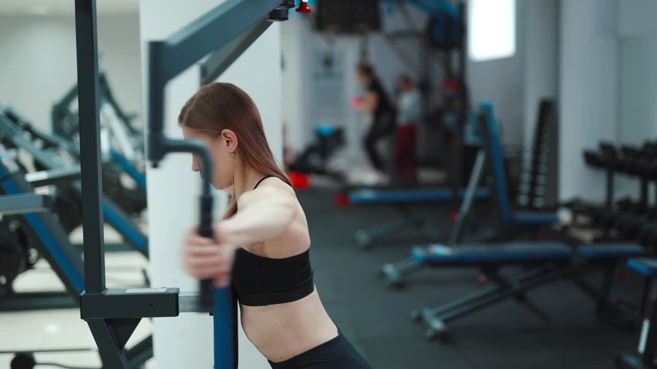 A strong young woman performs an exercise on the simulator for back and triceps. Blurred Background. Camera motion to right. Close-up