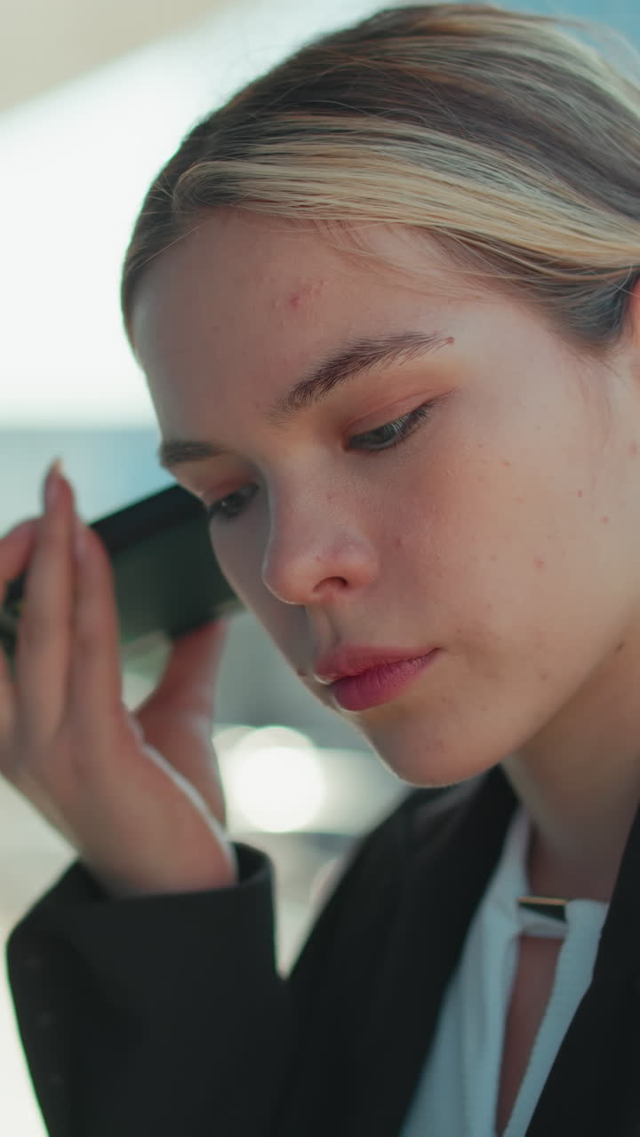 Close up of female lawyer attentively listening to voice note from client while standing outside modern glass building reflecting surroundings