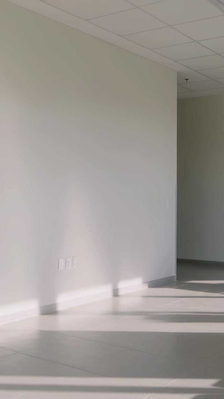 Vertical video: Panning camera revealing off white wall and sun patches on hall floor to show chair