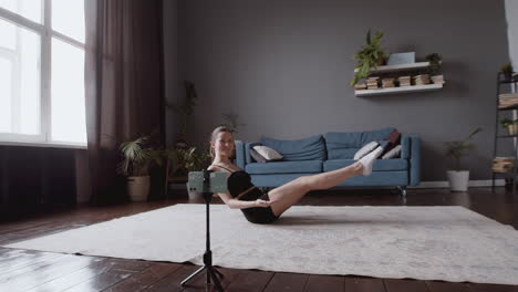 wide shot of an athletic female vlogger giving an online fitness class in front of her smartphone camera