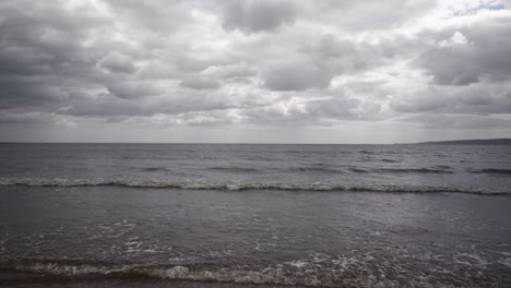 A-dramatic-skyline-over-the-sea-from-the-shoreline,-waves-lap-at-the-shore