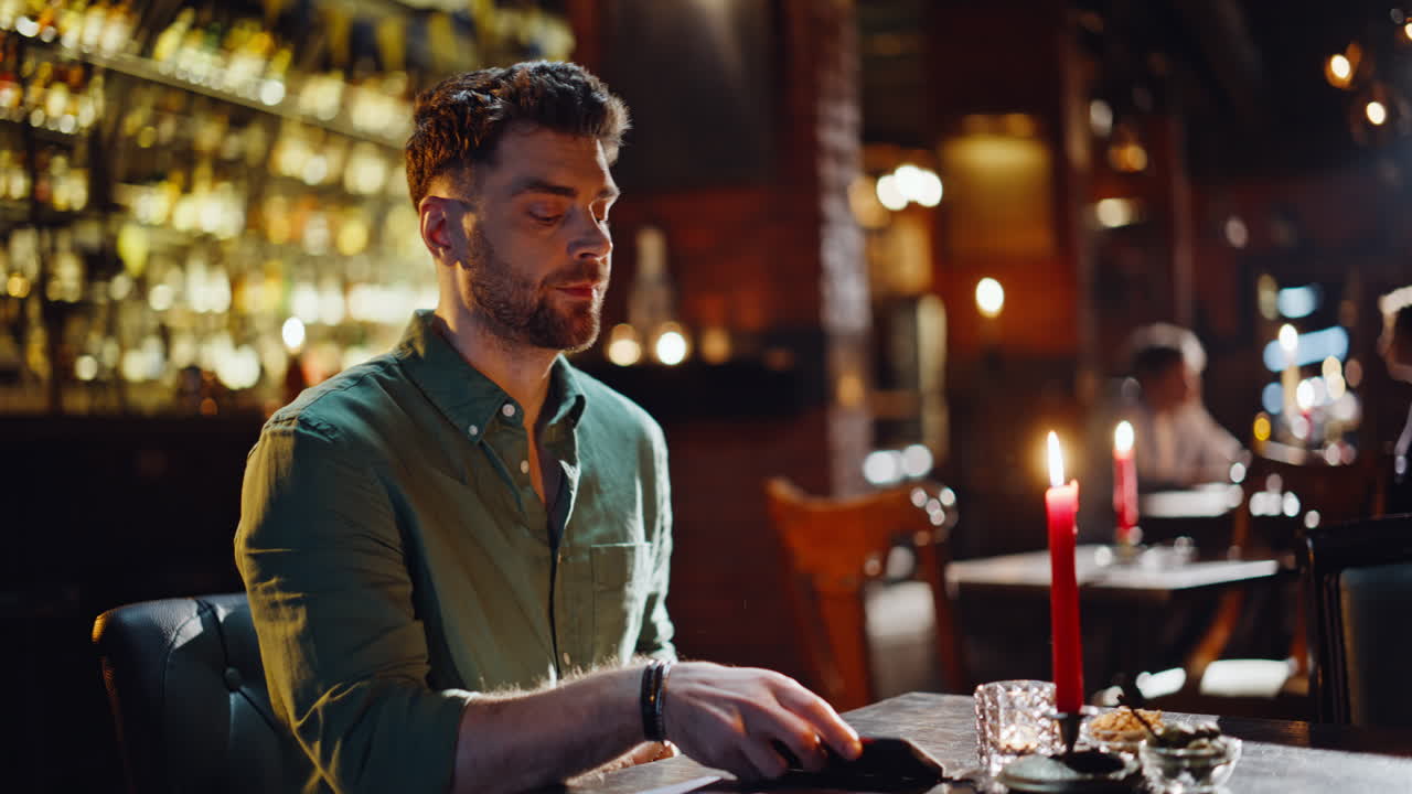 Primo piano di un hipster rilassato che controlla il telefono in un ristorante in attesa di un incontro romantico