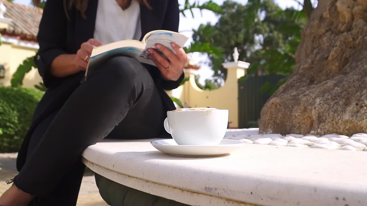 Jovem mulher profissional lendo um livro na natureza com uma xícara de café.