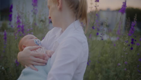 mother holding newborn near blooming flowers