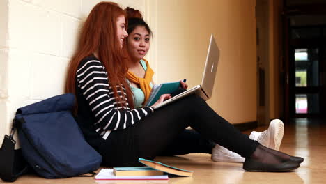 Pretty-students-chatting-in-corridor-using-laptop