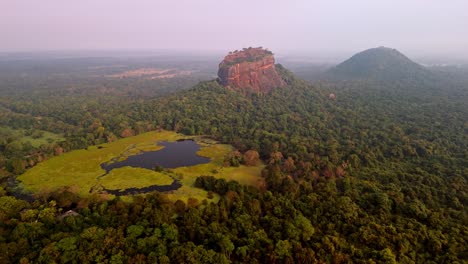 this cinematic drone footage showcases sri lanka’s iconic lion rock emerging through the mist, with warm golden hues bathing the ancient fortress and the wild, untouched nature around it.