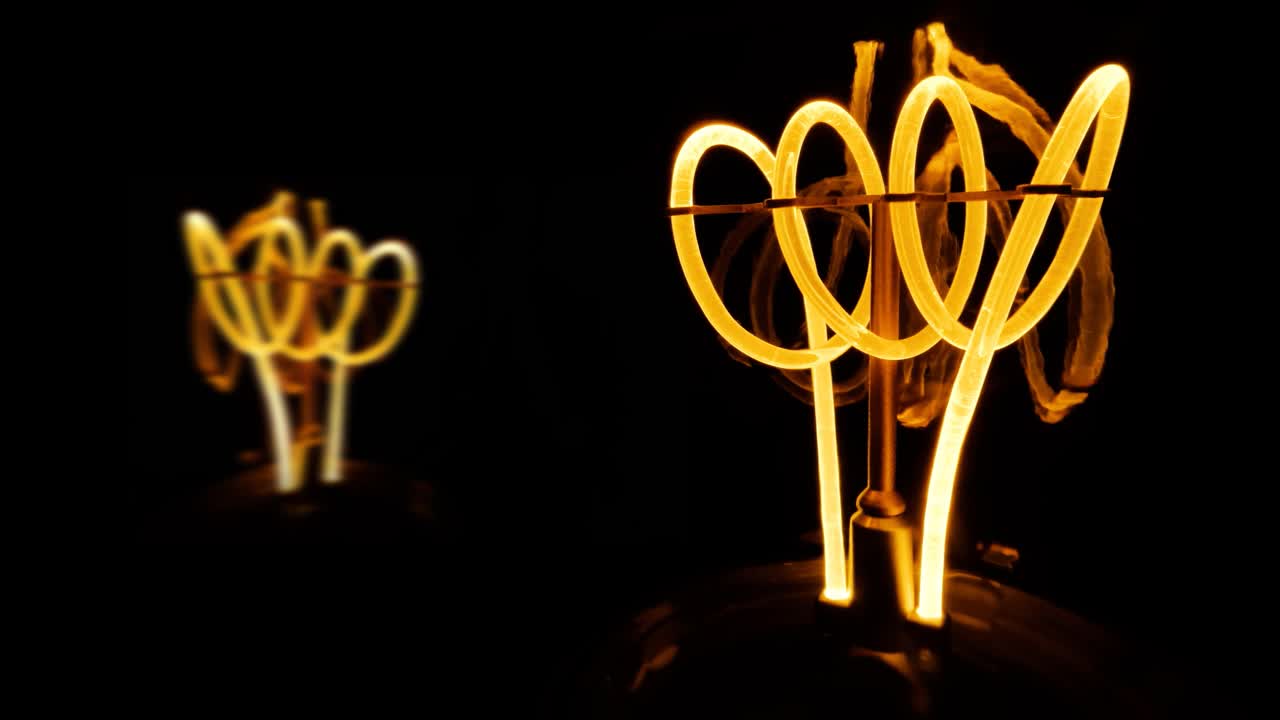 Lâmpadas de filamento de tungstênio cintilantes com uma espiral laranja em macro. Close-up de lâmpada espiral incandescente em fundo preto. Vídeo raw 4K em loop.