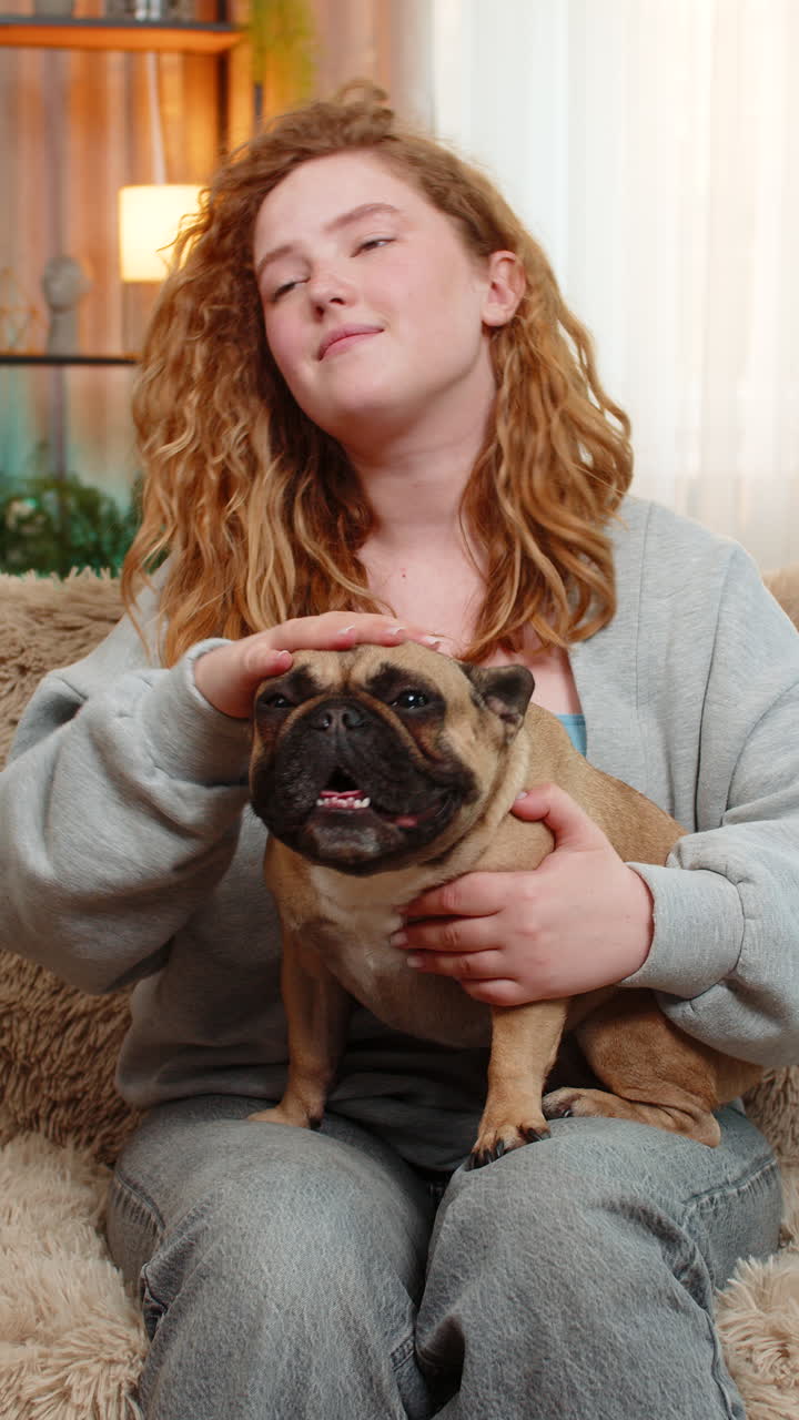 Young woman gently petting pug dog on home sofa with affection and calm expression in quiet moment