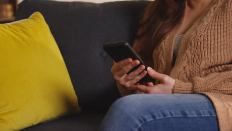 close up on hand of woman sitting on sofa at home using mobile phone to check social media message and scrolling online 3