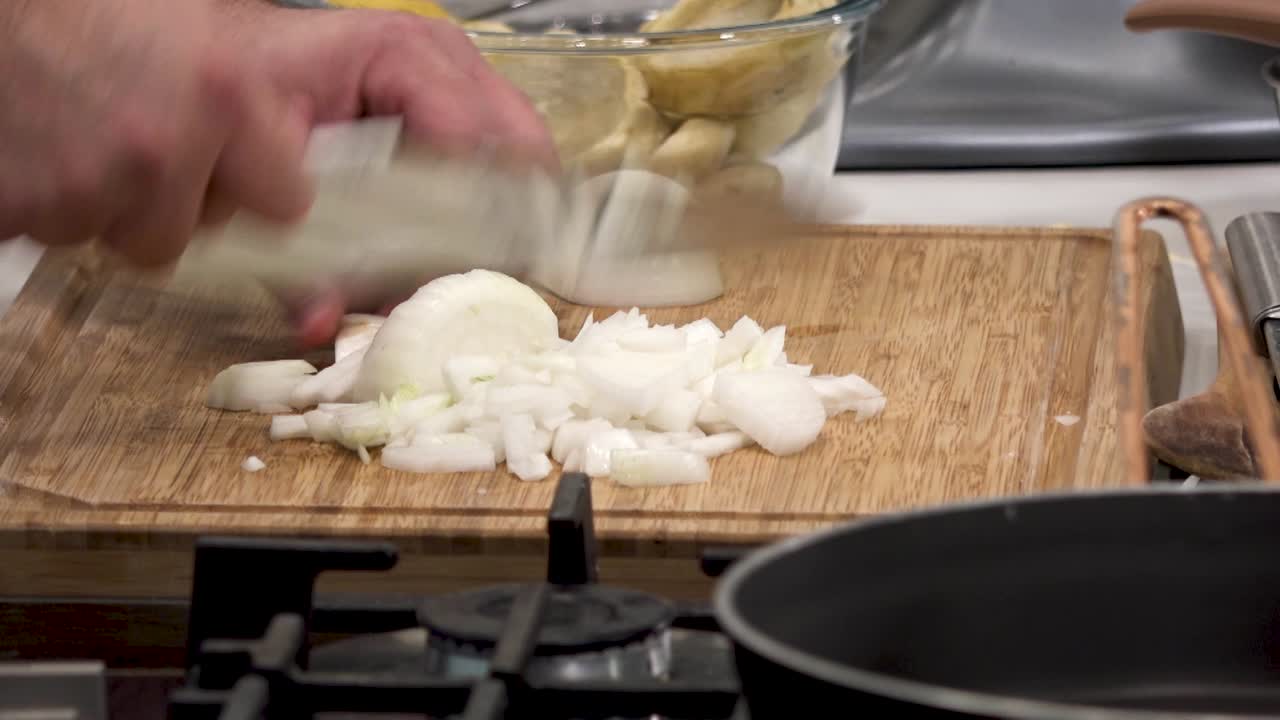 Hands skillfully chop onions on a cutting board while various vegetables are visible in the background, indicating a meal is being prepared in a kitchen