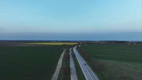 Vista-Cinematográfica-Aérea-De-Los-Coches-Que-Circulan-Entre-Los-árboles-Y-Los-Campos-En-La-Carretera-Rural-Con-Caminos-Rurales-Al-Lado