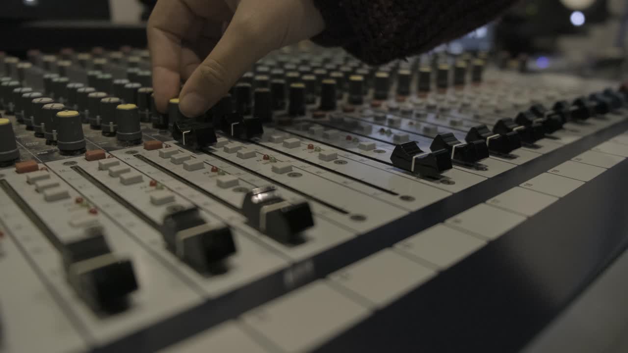 fingers moving sliders and turning the knobs on sound mixer console in recording studio