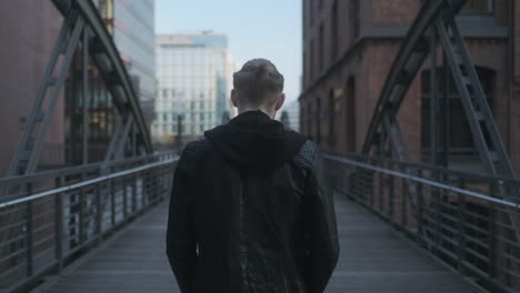 Young-European-Man-with-Leather-Jacket-and-Man-Bun-Walking-On-Bridge-in-Hamburg's-Tourist-Attraction-"Speicherstadt"