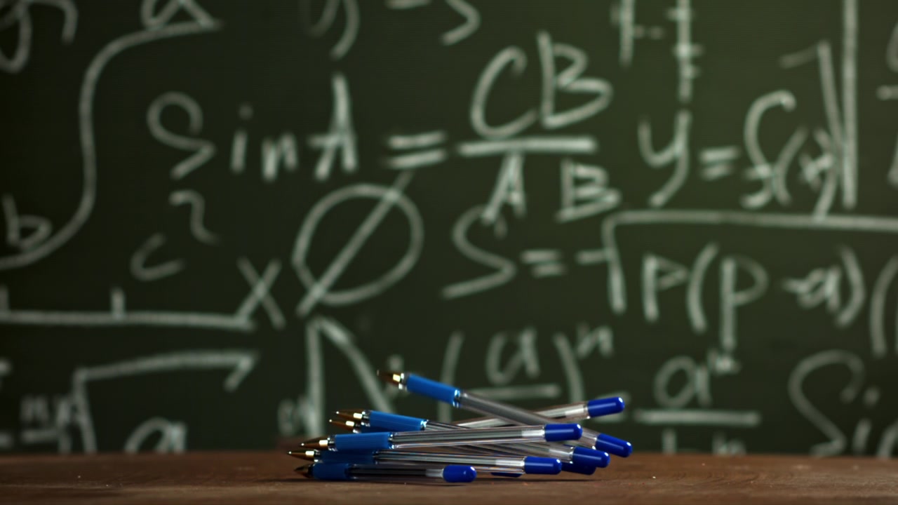 Blue Pens Falling in Slow Motion Against a Math Chalkboard