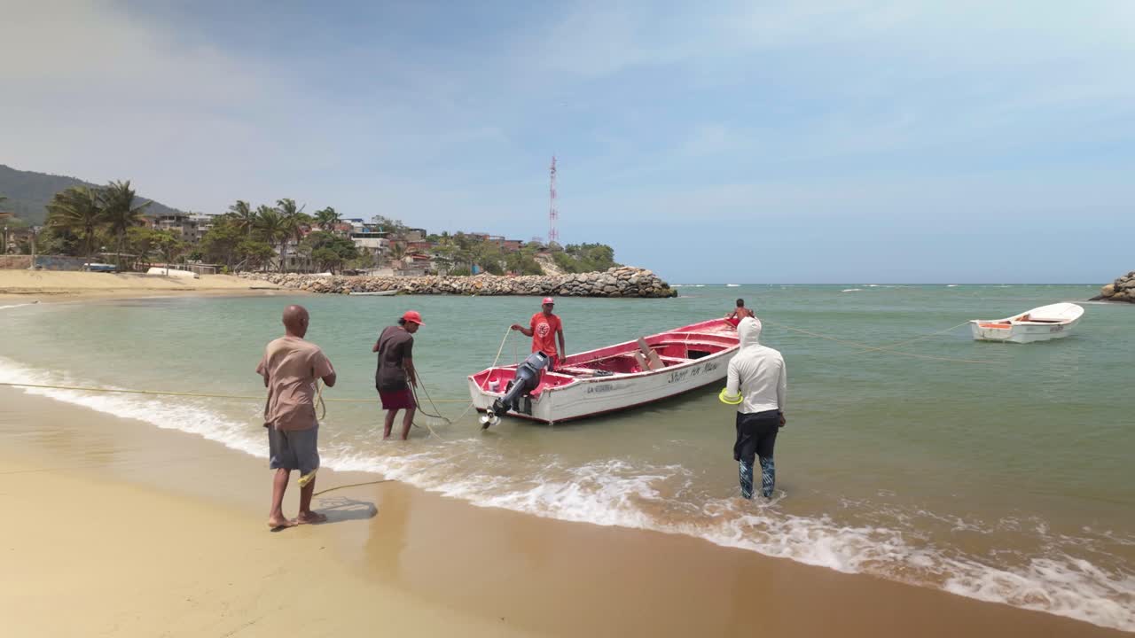 People are pulling a small red and white fishing boat onto sandy beach to go fishing, La Guaira