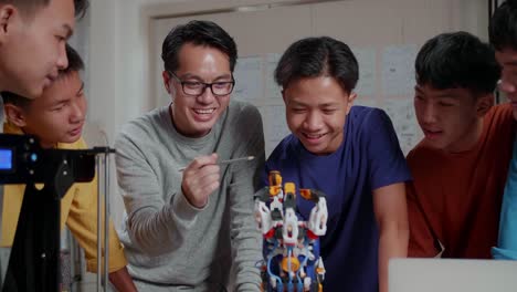 asian man with a laptop and 3d printing explaining about how to use a cyborg hand to the boys before celebrating the success at school