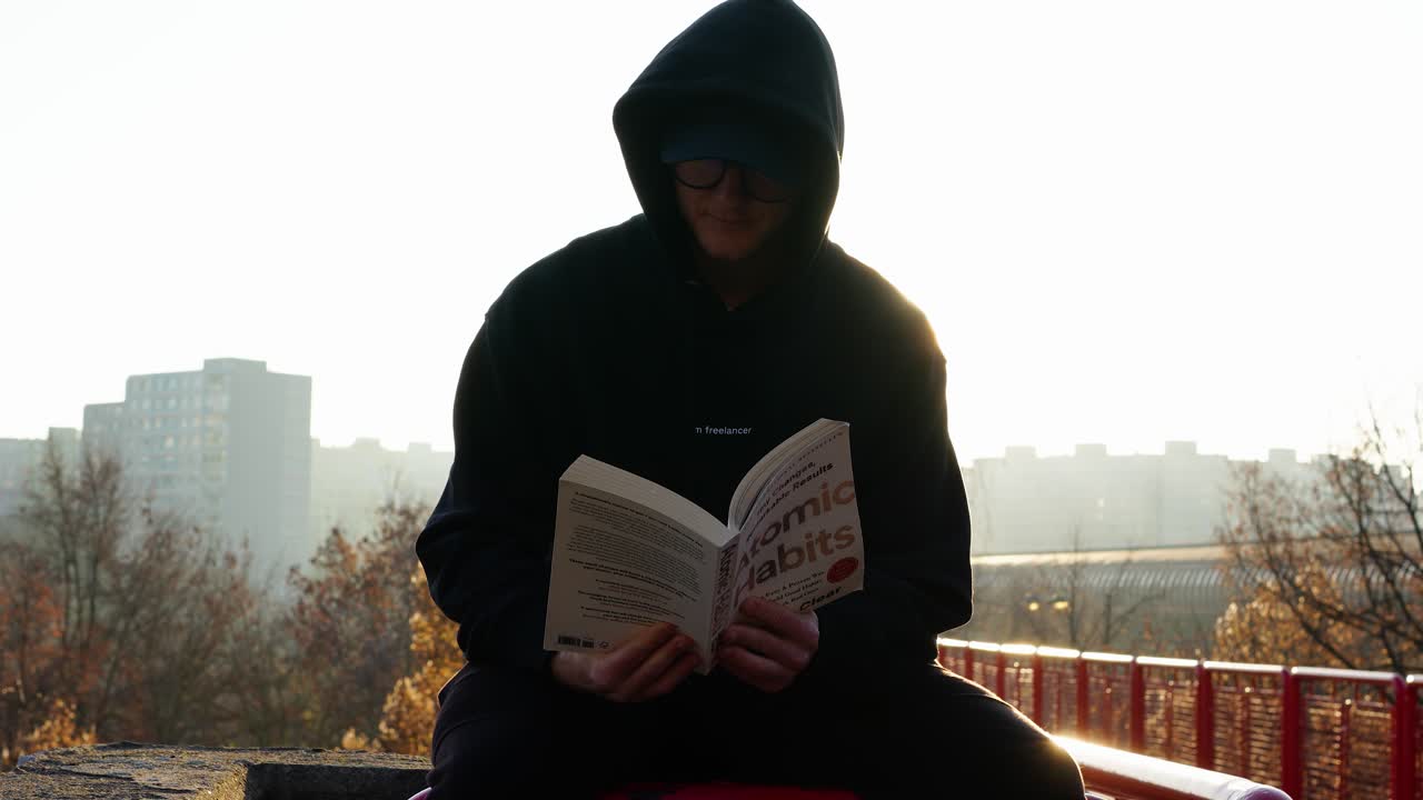 Person Reading Atomic Habits Book at Sunrise