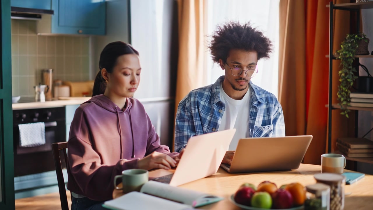 Diverse couple working laptops kitchen home. Freelancers studying morning.