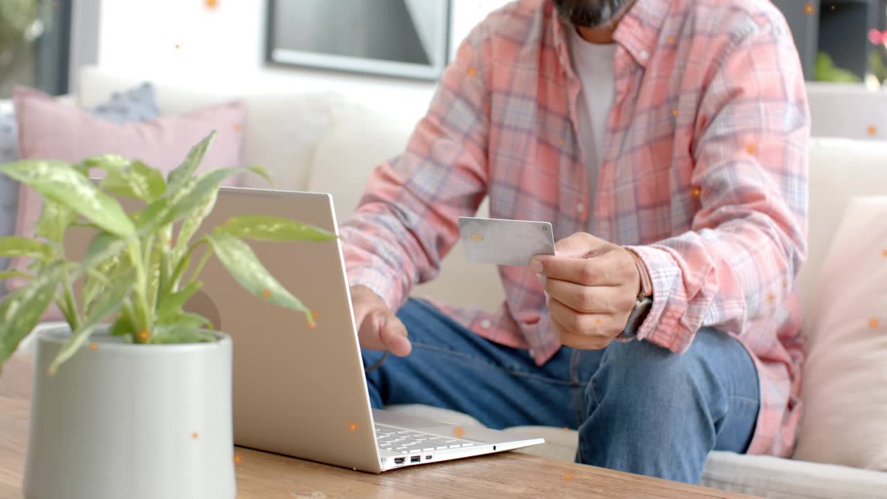Man holding card, inspecting it and typing on laptop, verifying online payment for finance task