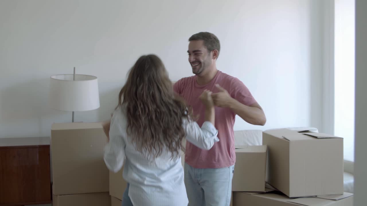 casal caucasiano feliz se mudando para uma casa nova, dançando e se divertindo na sala de estar com caixas