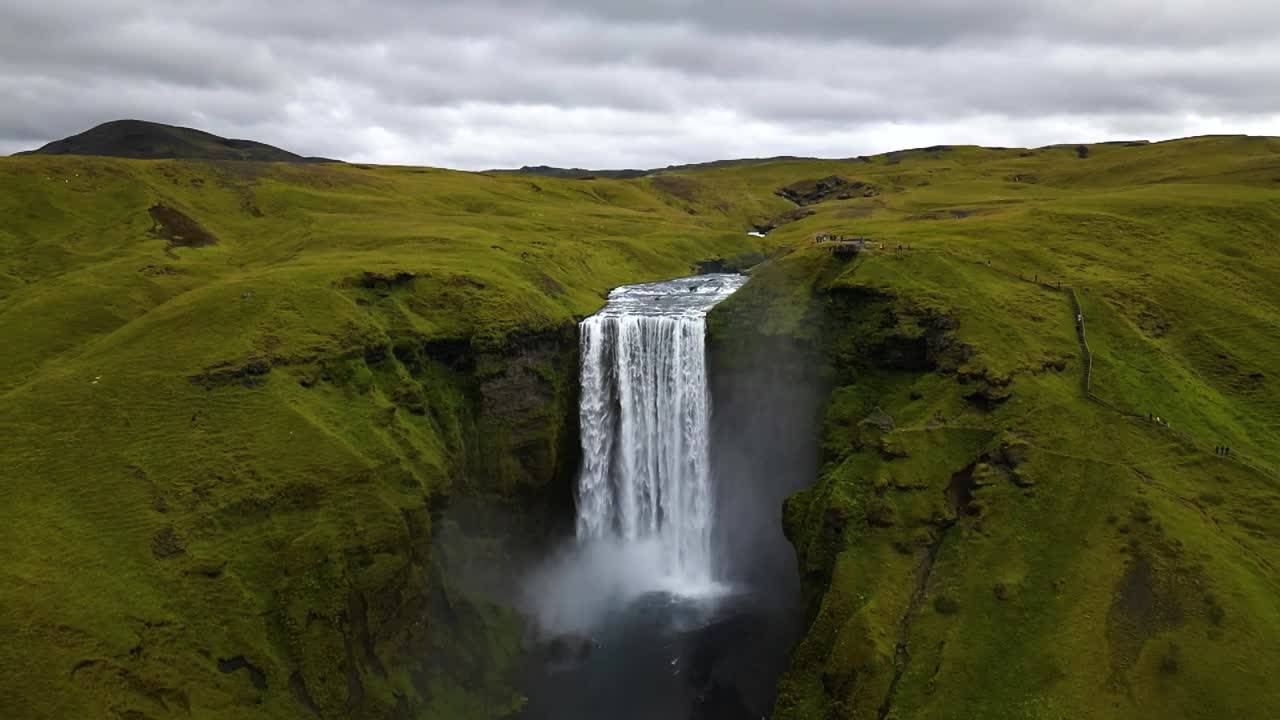 4K cinematic drone footage of Skógafoss Waterfall in Iceland, capturing the immense curtain of water cascading from towering cliffs surrounded by lush green landscapes. Iceland_26