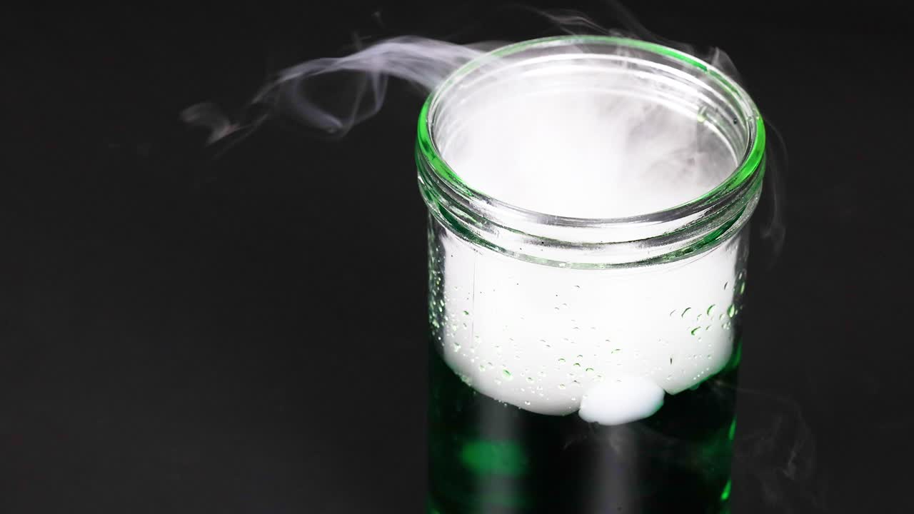 건조한 얼음이 들어있는 컵은 녹색 액체에서 안개 같은 반응을 일으켜 과학적 실험을 보여줍니다.