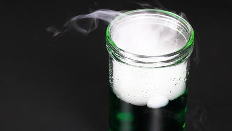 un vaso con hielo seco crea una reacción nebulosa en líquido verde, mostrando un experimento científico