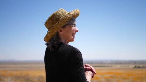 A-smiling-old-woman-with-gray-hair-laughing-in-a-summer-field-of-orange-flowers-under-blue-sky-SLOW-MOTION