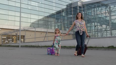 Mother-and-daughter-walking-from-airport.-Woman-and-child-carrying-suitcase-bags.-Mom-after-vacation