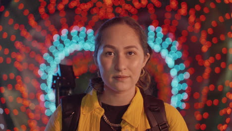 Close-up-Portrait-Of-A-Woman-With-Colorful-Heart-String-Light-Display-In-Background