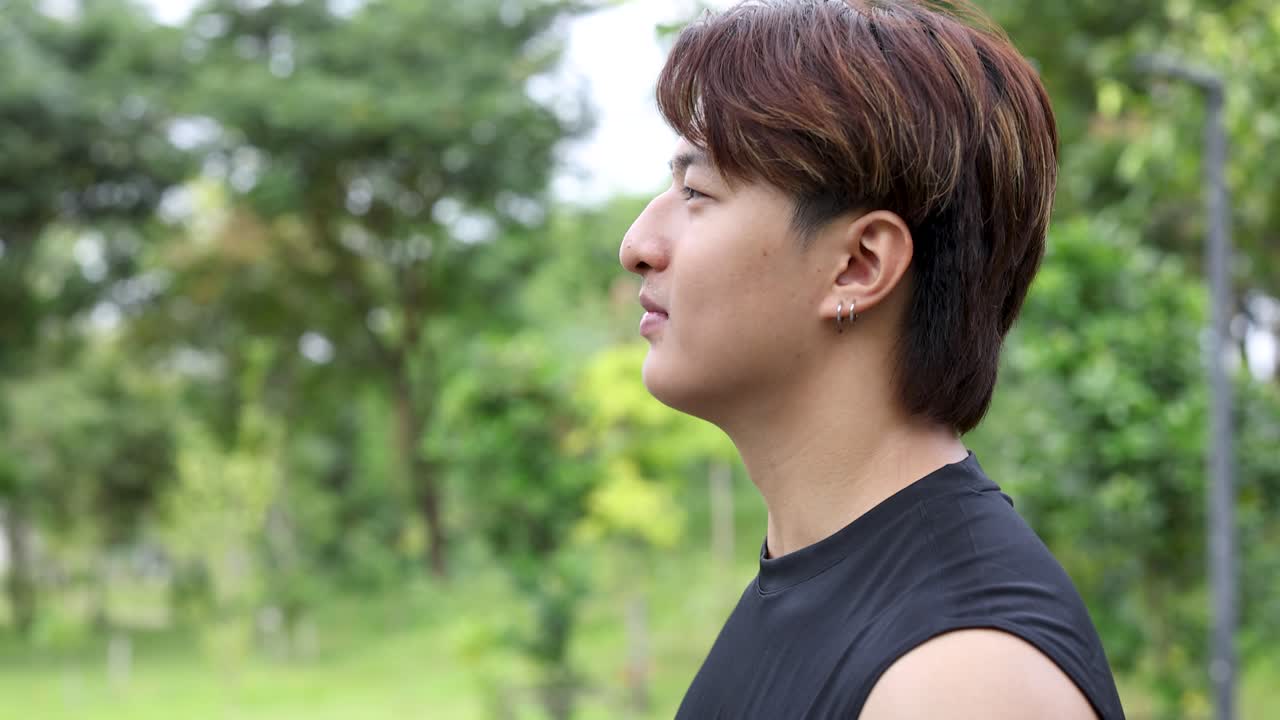 A fit young man walks through a lush green park during a bright daylight workout