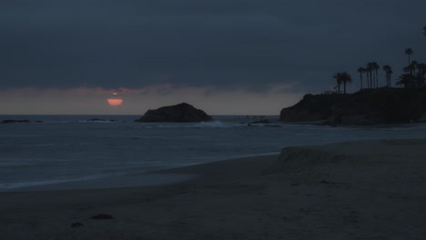 timelapse of the sun setting behind ocean cliffs and swaying palms, casting a golden glow over the beach as evening falls on a tranquil coastal scene.
