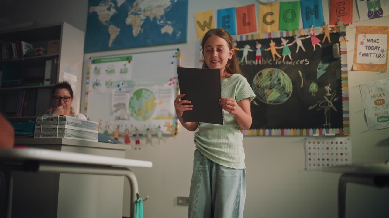 Muslim Primary School Girl Wearing Hijab Sitting at the Desk Writing School Test in Notebook