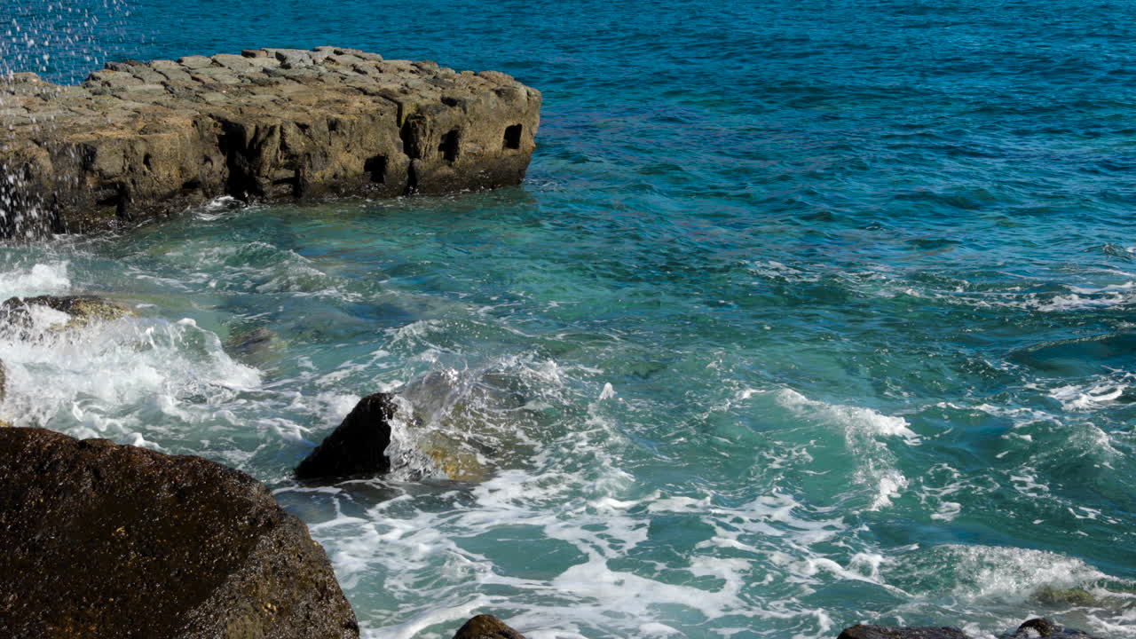 Azure sea as the water strikes a rocky coastline full of stones and a shore that reflects and breaks in all directions 4k slow motion capture at 60fps