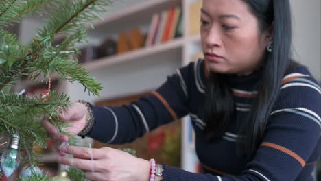 an asian woman takes christmas decorations off the tree after the holidays