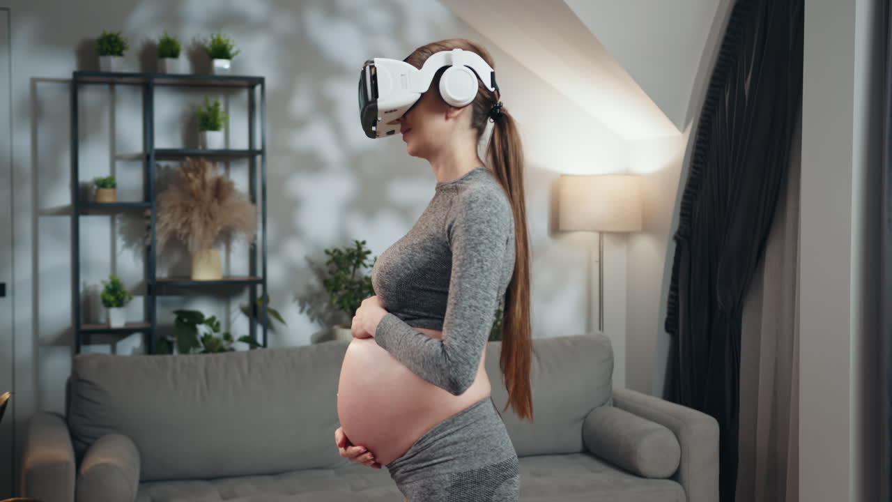 Femme enceinte portant un casque de réalité virtuelle et des écouteurs, touchant son ventre en position debout