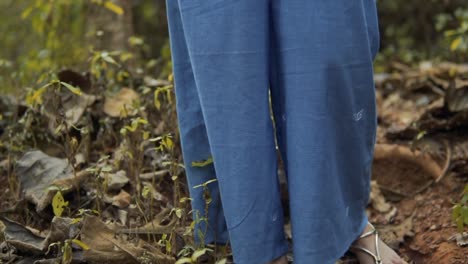 un jeune adolescent porte un pantalon bleu debout sur une tige de feuille séchée derrière un environnement vert