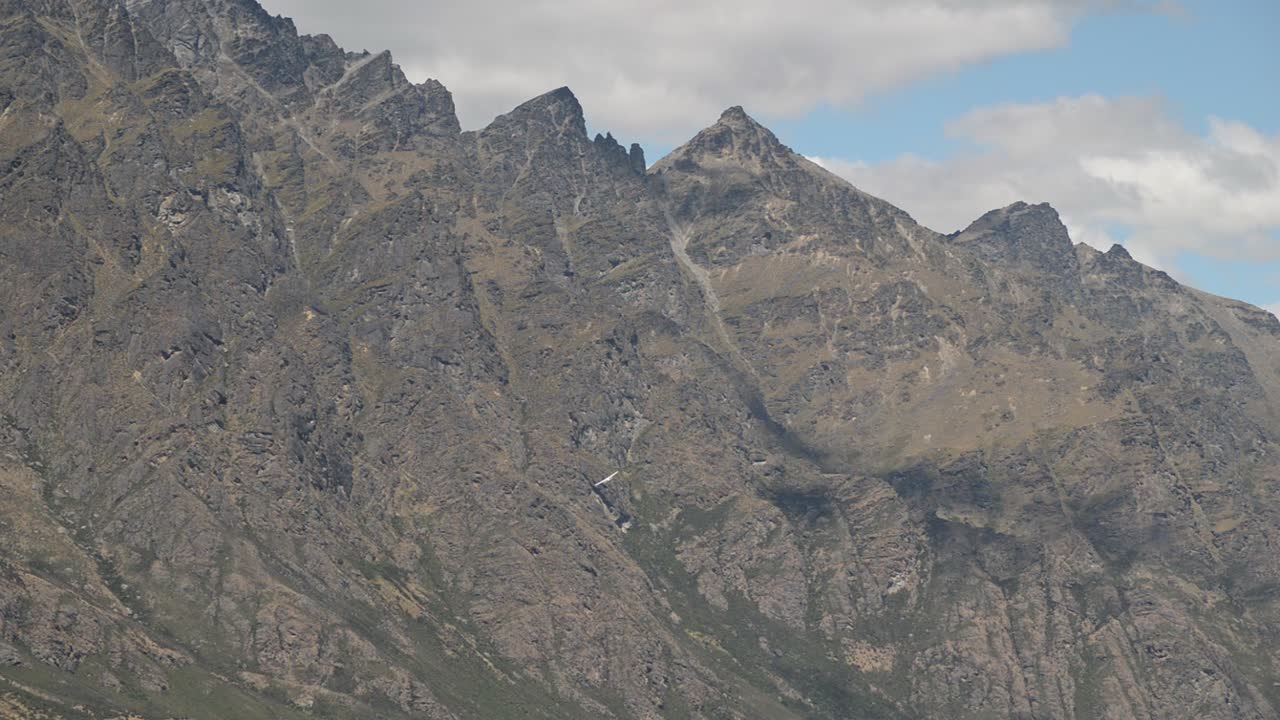 Winziges Flugzeug dreht sich vor riesiger, zerklüfteter Klippe.