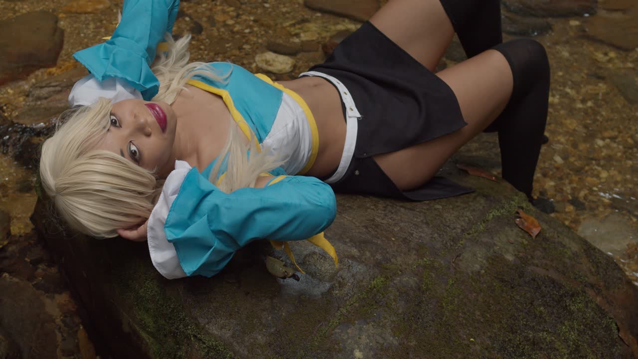 aguas cristalinas que fluyen de una cascada mientras un cosplayer de anime se acuesta en las rocas y sonríe