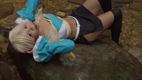 Aguas-Cristalinas-Que-Fluyen-De-Una-Cascada-Mientras-Un-Cosplayer-De-Anime-Se-Acuesta-En-Las-Rocas-Y-Sonríe