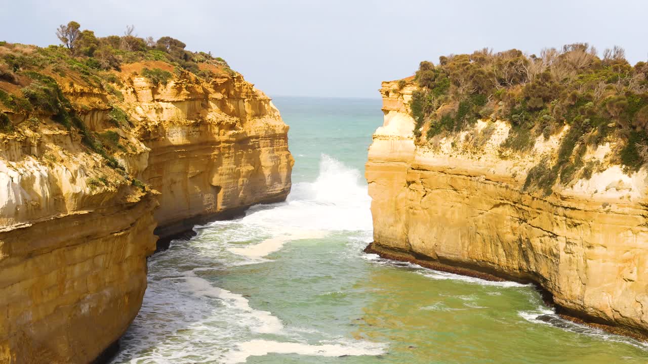 Dynamic ocean waves crash against the rugged cliffs of Loch Ard Gorge, captured in bright daylight with steady camera movement