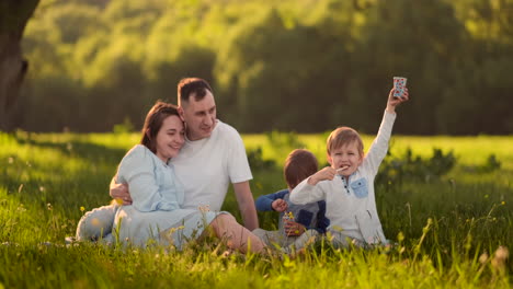 Liebevolle-Eltern-Sitzen-Umarmend-Bei-Sonnenuntergang-Auf-Dem-Feld-Und-Schauen-Lächelnd-Ihren-Beiden-Söhnen-Zu,-Die-Im-Sommer-Ein-Eis-Essen.