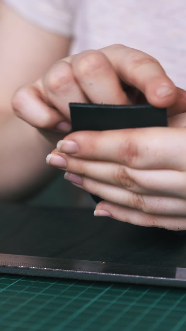 CU: Experienced designer polishes black leather strip edge with brown wooden slicker in workshop close view