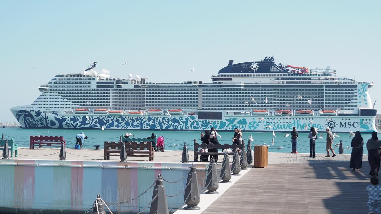 Large MSC cruise ship docked at a sunny pier with people and birds