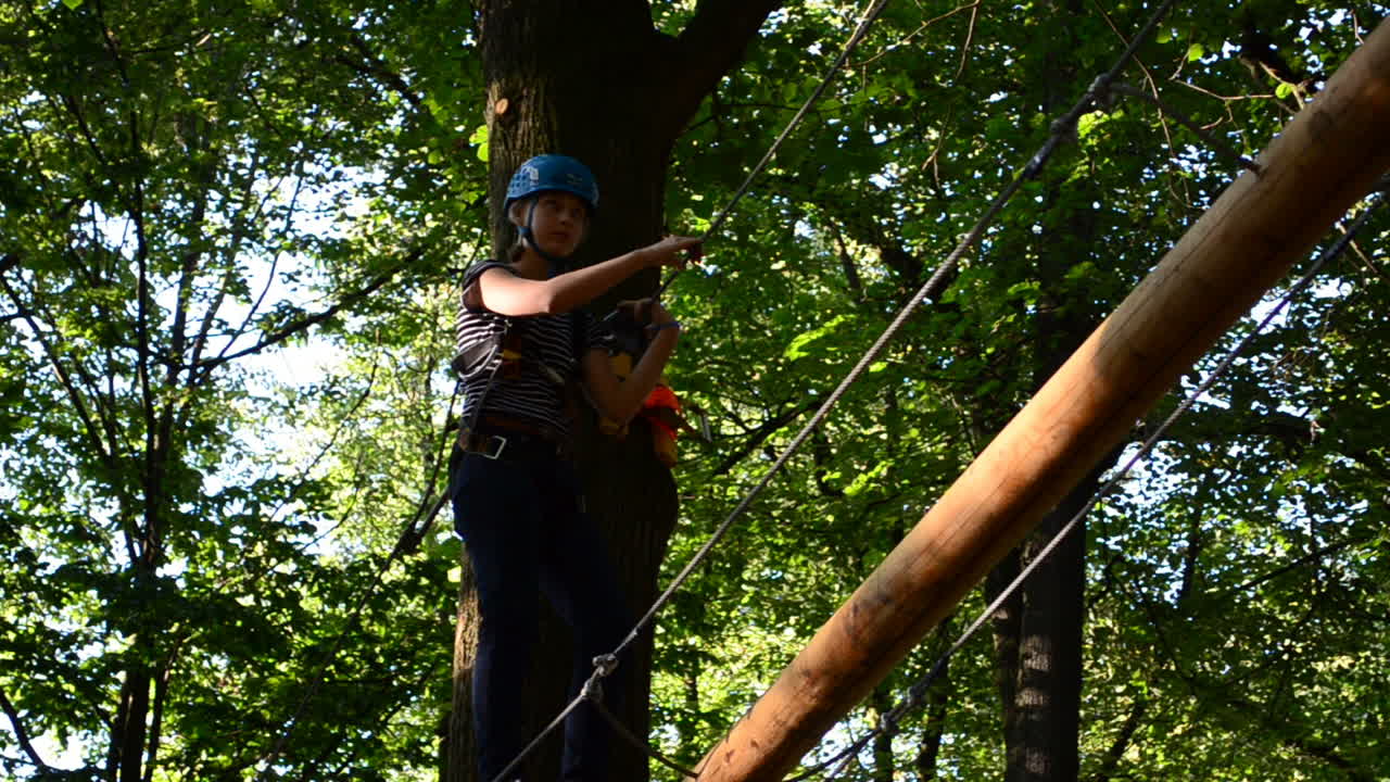 The girl the teenager overcomes obstacles between trees at height. Shooting in the summer